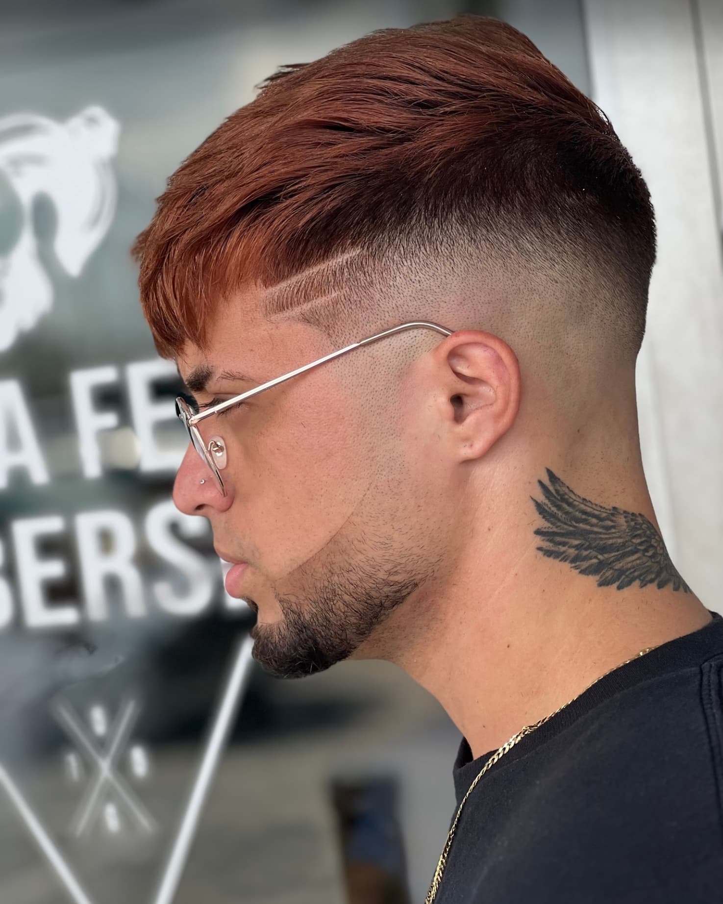 Skin fade con lineas en la sien frente al letrero de La Fe Barbershop